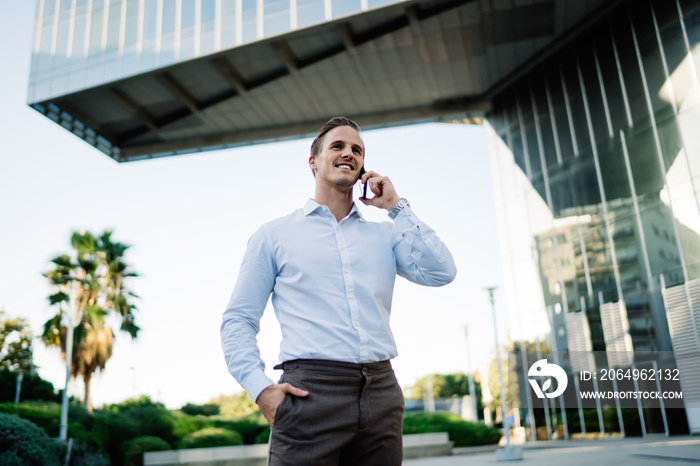 Smiling male director holding hand in pocket while answering phone call in downtown