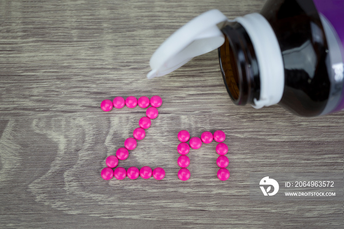 Pink pills forming shape to Zn alphabet on wood background