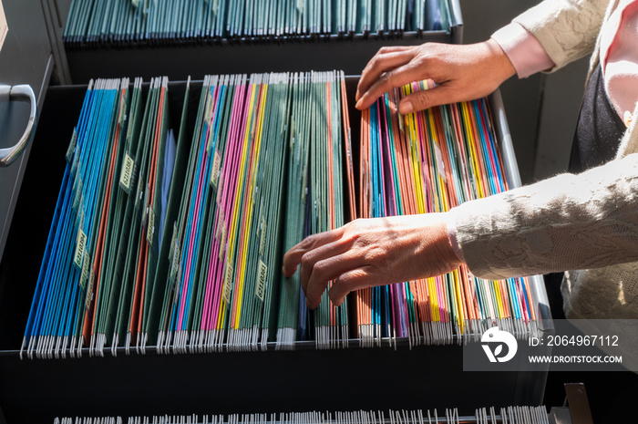 Working women search for colorful files, sorted in filing cabinets.