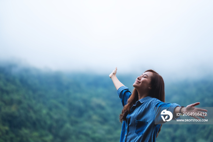 雾天，一位女旅行者闭上眼睛，张开双臂，身后是美丽的青山