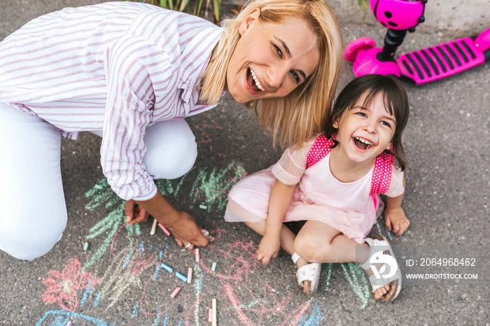快乐微笑的小女孩和母亲在人行道上笑着用粉笔画画。高加索fem