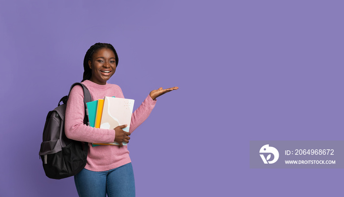 Smiling african female student pointing aside at copy space on purple background