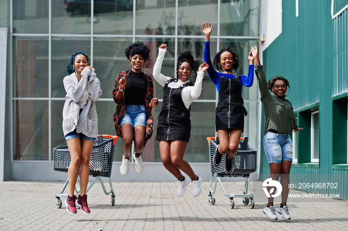 五名非洲裔美国妇女组成的小组，带着购物车，一起玩得很开心，在户外跳跃。