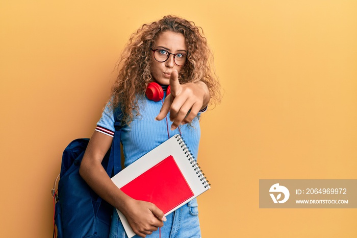 Beautiful caucasian teenager girl wearing student backpack and holding books pointing with finger to