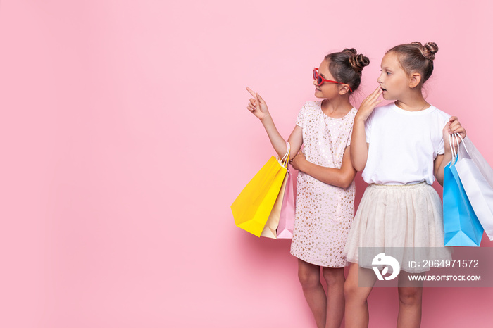 Two smiling teenage girls hold bags in their hands after a shopping trip, looking at empty space