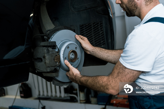 cropped view of bearded car mechanic holding metallic car brake near automobile