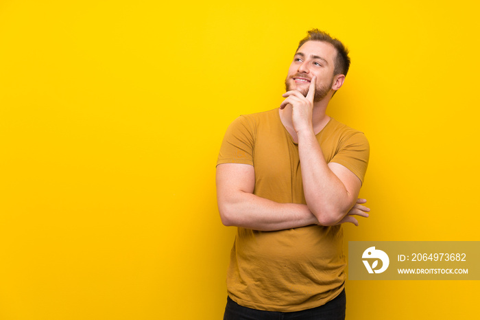 Blonde man over isolated yellow wall thinking an idea while looking up