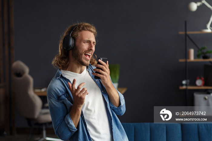 Handsome long haired curly man with headphones listening music,singing and dancing.Funny emotional s