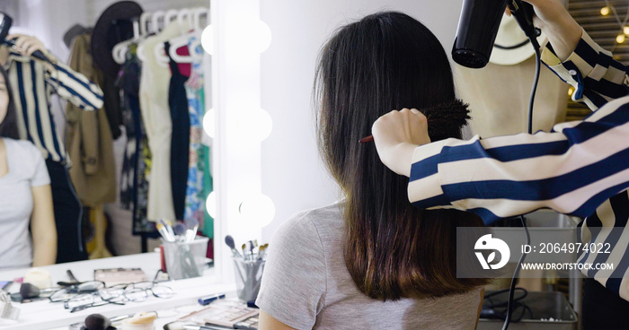 female hairdresser dries black short hair with hairdryer in backstage dressing room for fashion show