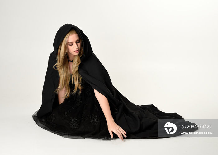 full length portrait of blonde girl wearing long black flowing cloak, sitting on the floor  with  a 