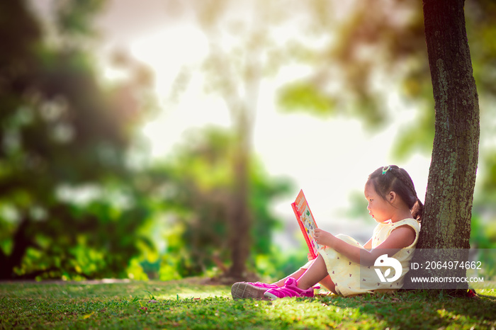 一个穿着黄色连衣裙的可爱小女孩坐在树下看书