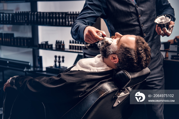 Barber applies shaving foam to a mans face in a saloon.