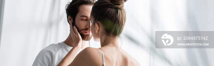 back view of woman hugging bearded man with closed eyes at home, banner.