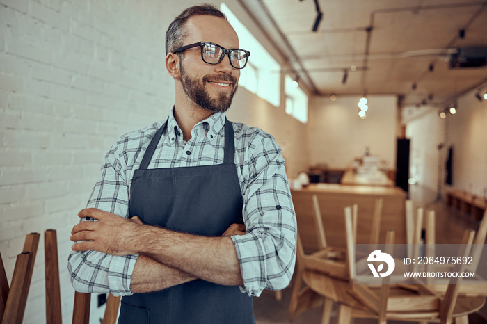 Joyful bearded man in apron standing in cafe