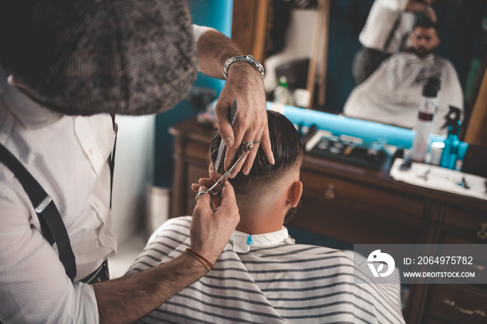 Professional hairdresser doing haircut with scissors in barbershop