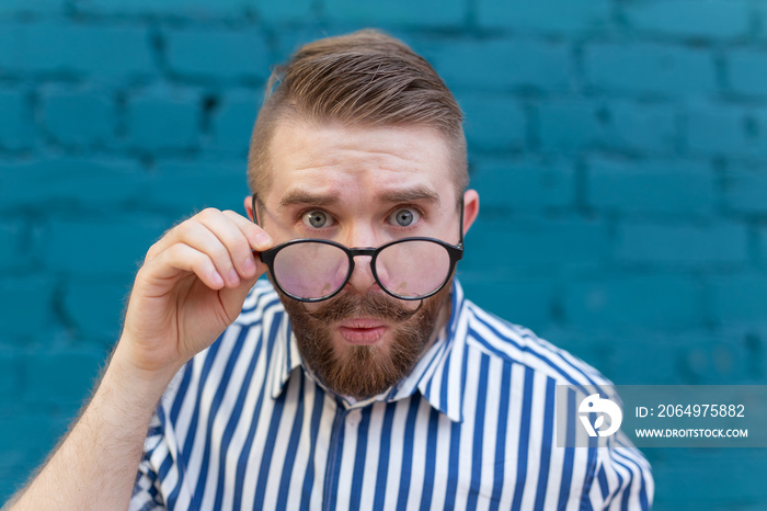 Close-up portrait of a curious surprised young man in glasses with a mustache and beard posing on a 