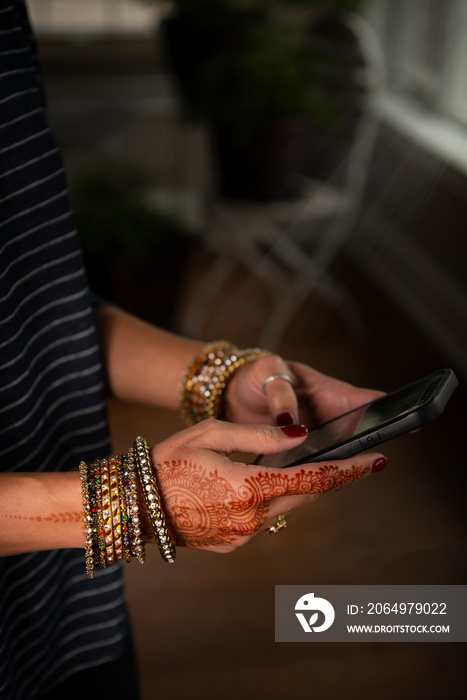 Womans hands with henna typing on phone