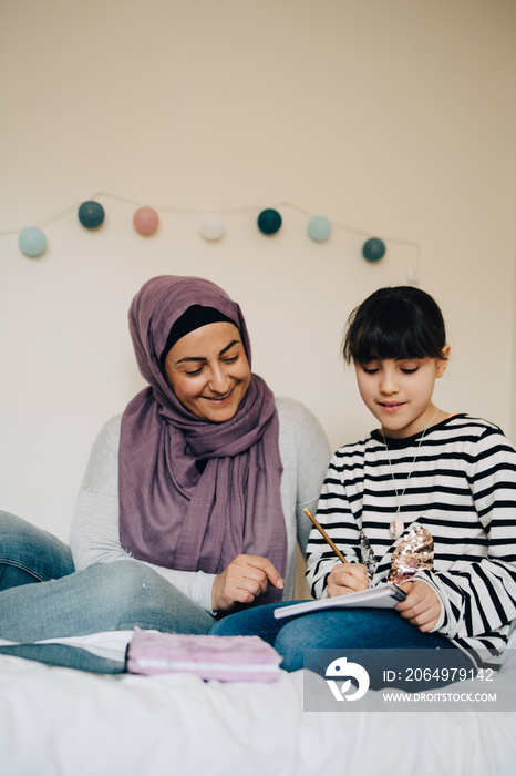 Mature woman assisting daughter in homework on bed at home