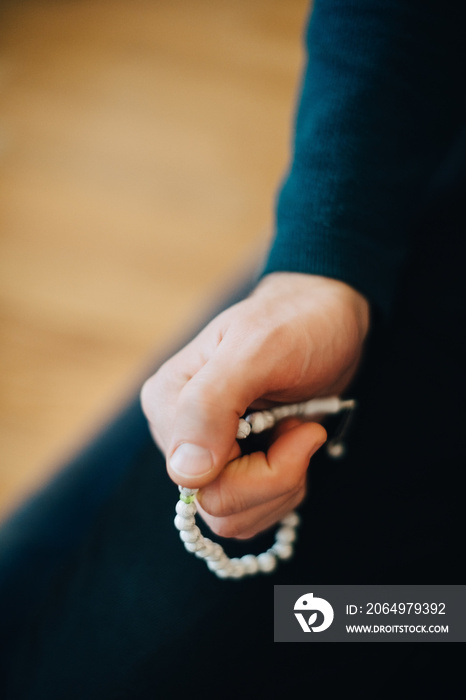 Cropped image of man praying with rosary beads at home