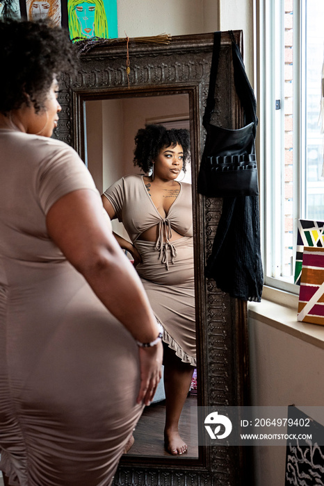 Black woman wearing brown dress looking in the mirror