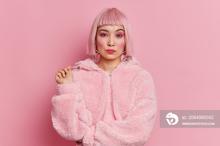严肃漂亮的亚洲女人，留着时髦的粉红色头发，穿着冬季外套，化着鲜艳生动的妆