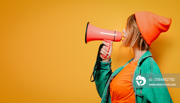 Young style girl in jeans clothes with pink megaphone on yellow background. Symbolizes female resist