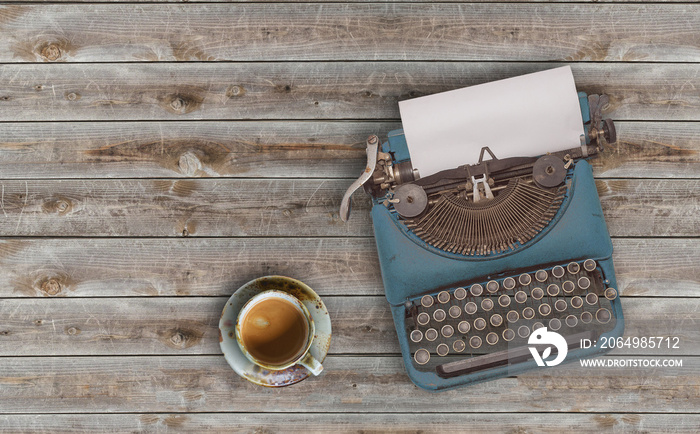 top view photo of vintage typewriter with blank page next to cup of coffee, on wooden table.