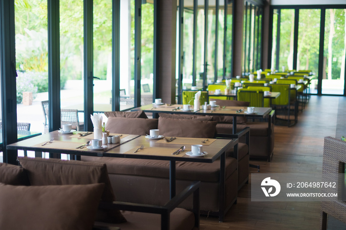 Empty restaurant part of hotel with table and armchair near windows and garden view.