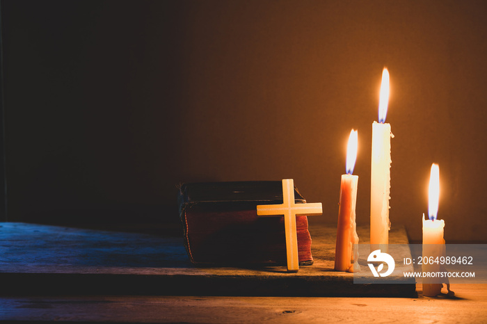 Cross with bible and candle on a old oak wooden table. Beautiful gold background. Religion concept.