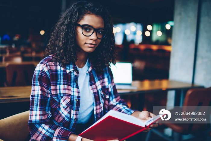 Portrait of beautiful smart african american student with curly hair and eyeglasses looking at camer