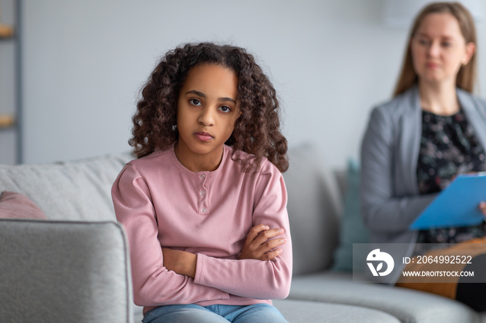 Psychological help and assistance. Sad teen girl sitting back to doctor, looking at camera