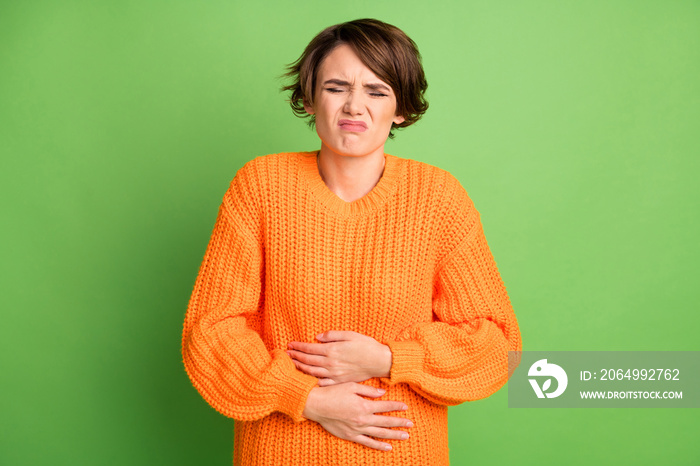 Portrait of sad nice brunette lady stomach pain wear orange sweater isolated on pastel green backgro