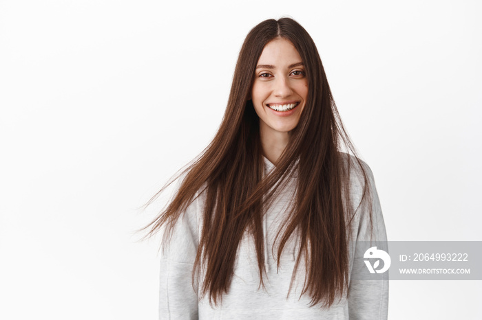 Beauty. Attractive young brunette woman smiling happy, shiny long hair flying in air on wind, hairca