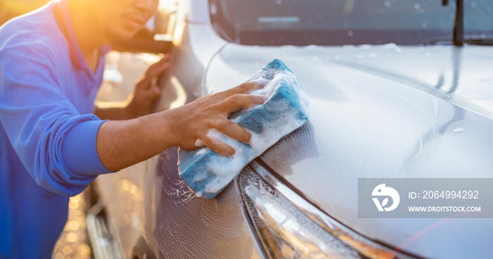 日落时分，一名亚洲男子在户外用蓝色海绵和肥皂洗车
