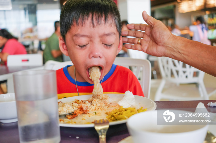 Boy puking on plate after having lunch meal in food court with helping hand