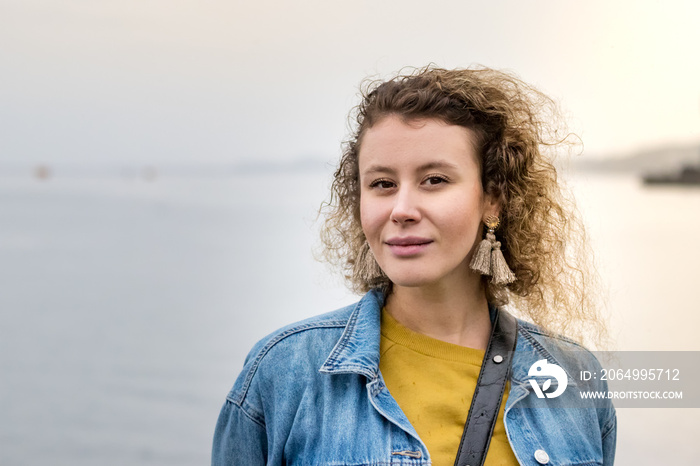 Portrait of a young woman with curly hair looking camera dreaming, confident, outdoors.