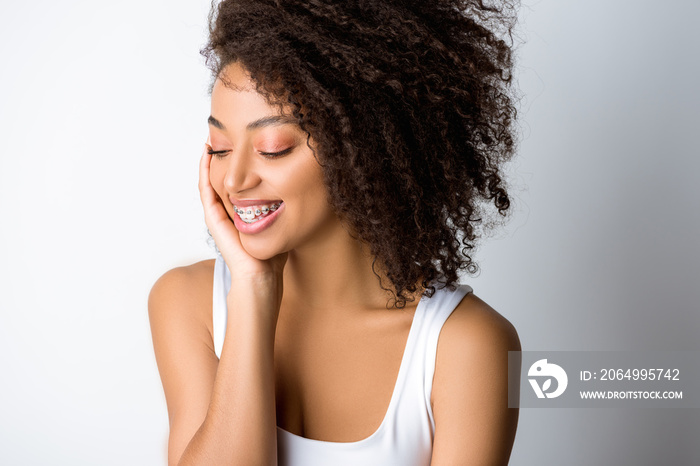 smiling curly african american girl with dental braces, isolated on grey