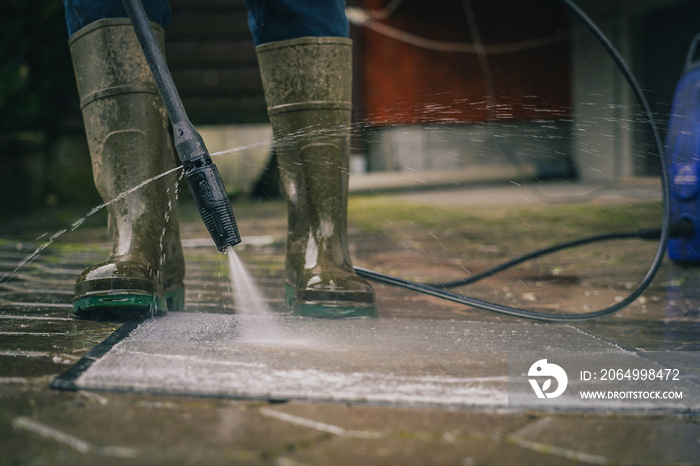 Person cleaning a rug or floor mat with the use of a high pressure water cleaner. Cleaning mats with