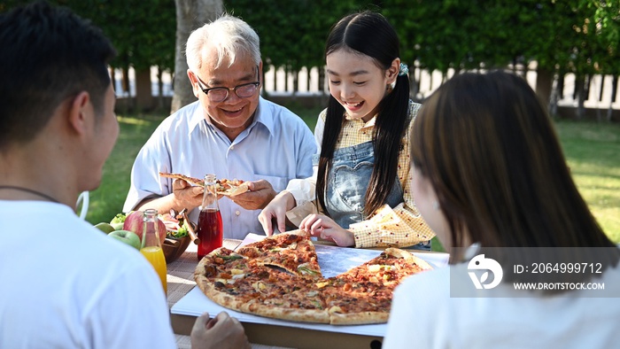 Asian family having pizza in garden at home. Parent with kid and grandfather lifestyle in backyard.