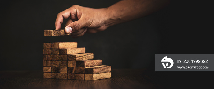 Close-up hand is placing wood block tower stacked in pyramid stair step with caution to prevent coll