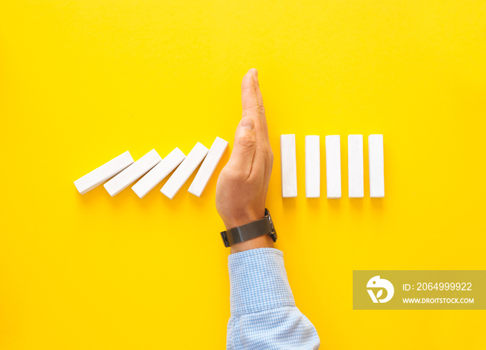 Businessman hand stopping falling dominos on yellow background. Business management crisis concept.