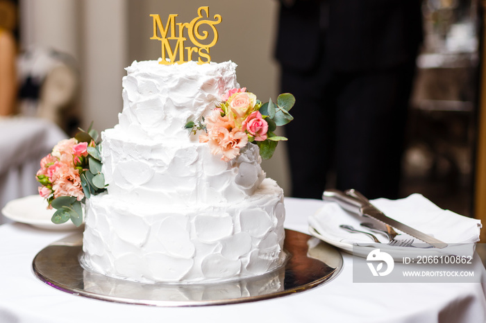 一个多层白色婚礼蛋糕，底部为银色，顶部为粉色花朵