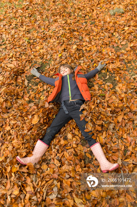 Playful girl laying in autumn leaves