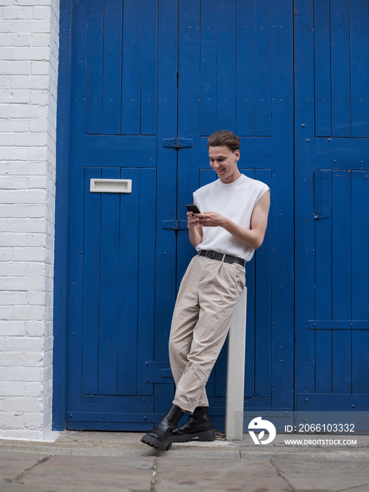 Young man standing against blue doors and using smart phone