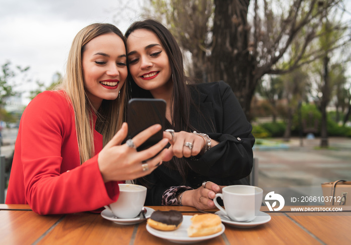 Two friends using their mobile phone while sitting at coffee shop.