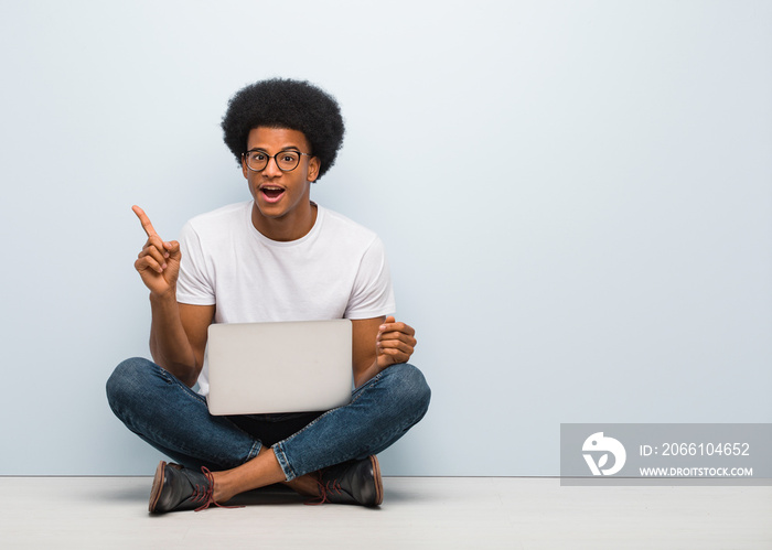 Young black man sitting on the floor with a laptop pointing to the side