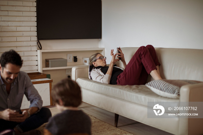 Boy playing with father while grandmother using mobile phone in living room