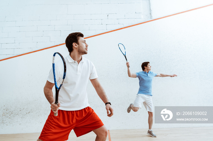 Two sportsmen playing squash with rackets in four-walled court