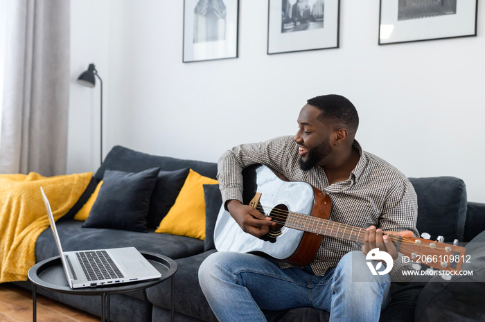 Young African American male musician or teacher playing guitar during an online concert lesson at ho