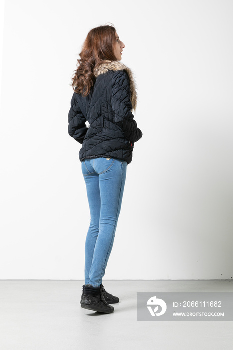 Full length portrait of a girl wearing simple blue jacket and jeans, standing pose facing away on a 